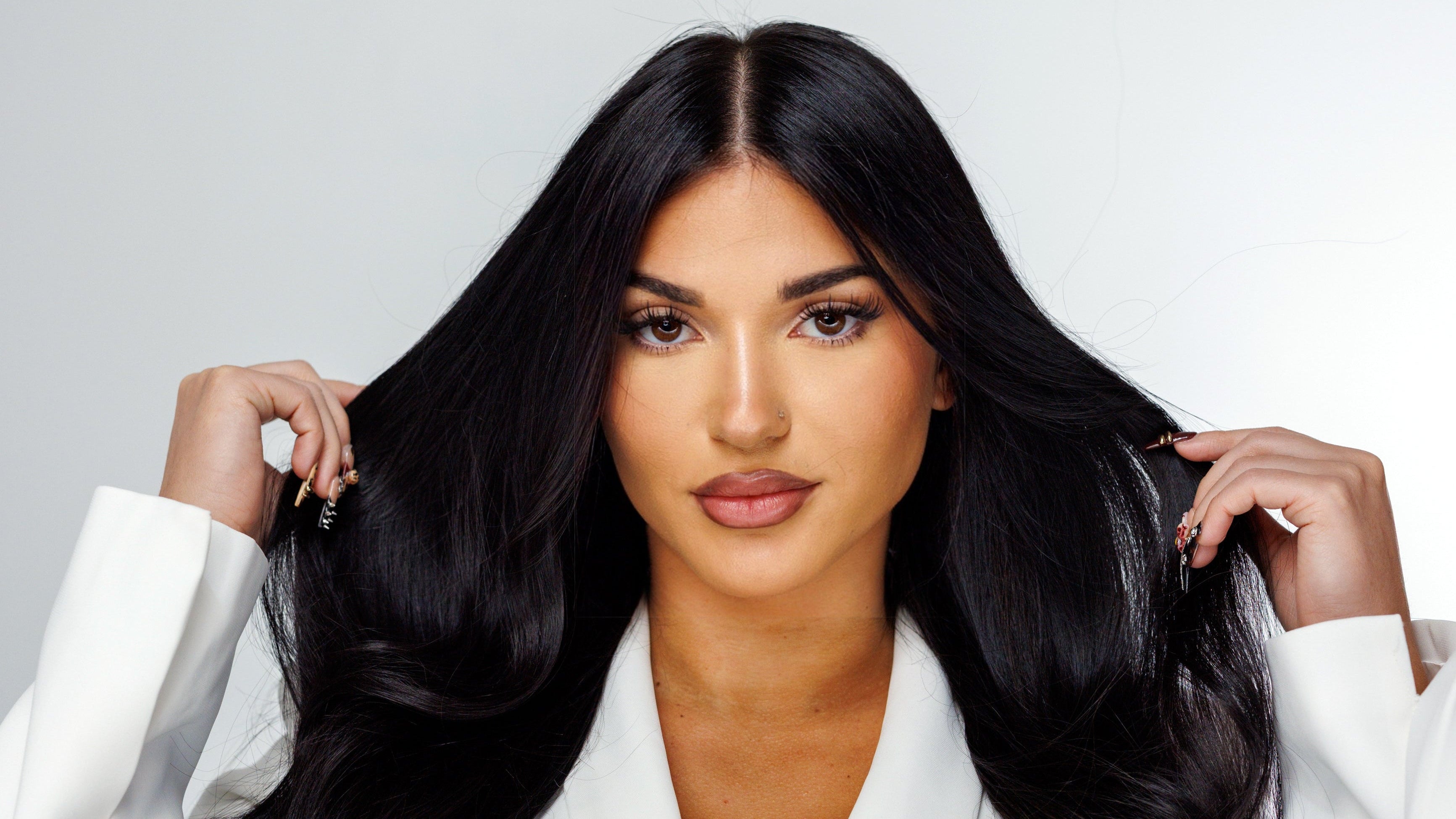 Woman with long, straight black hair wearing a white robe against a light gray background dark black hair extensions done by your favorite salon in downtown orlando jazmyn nyx